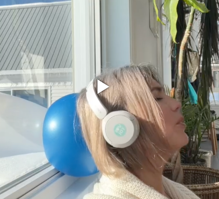 Person wearing headphones with a blue balloon and plant in the background
